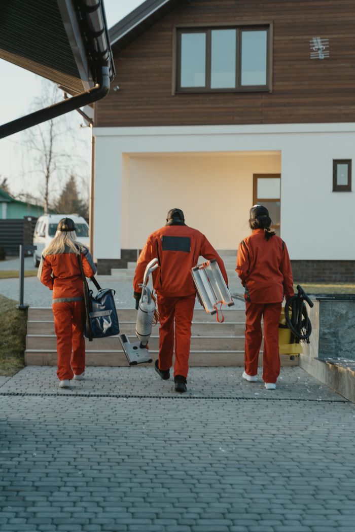 A cleaning team in red uniforms, carrying equipment as they head toward a modern home exterior.